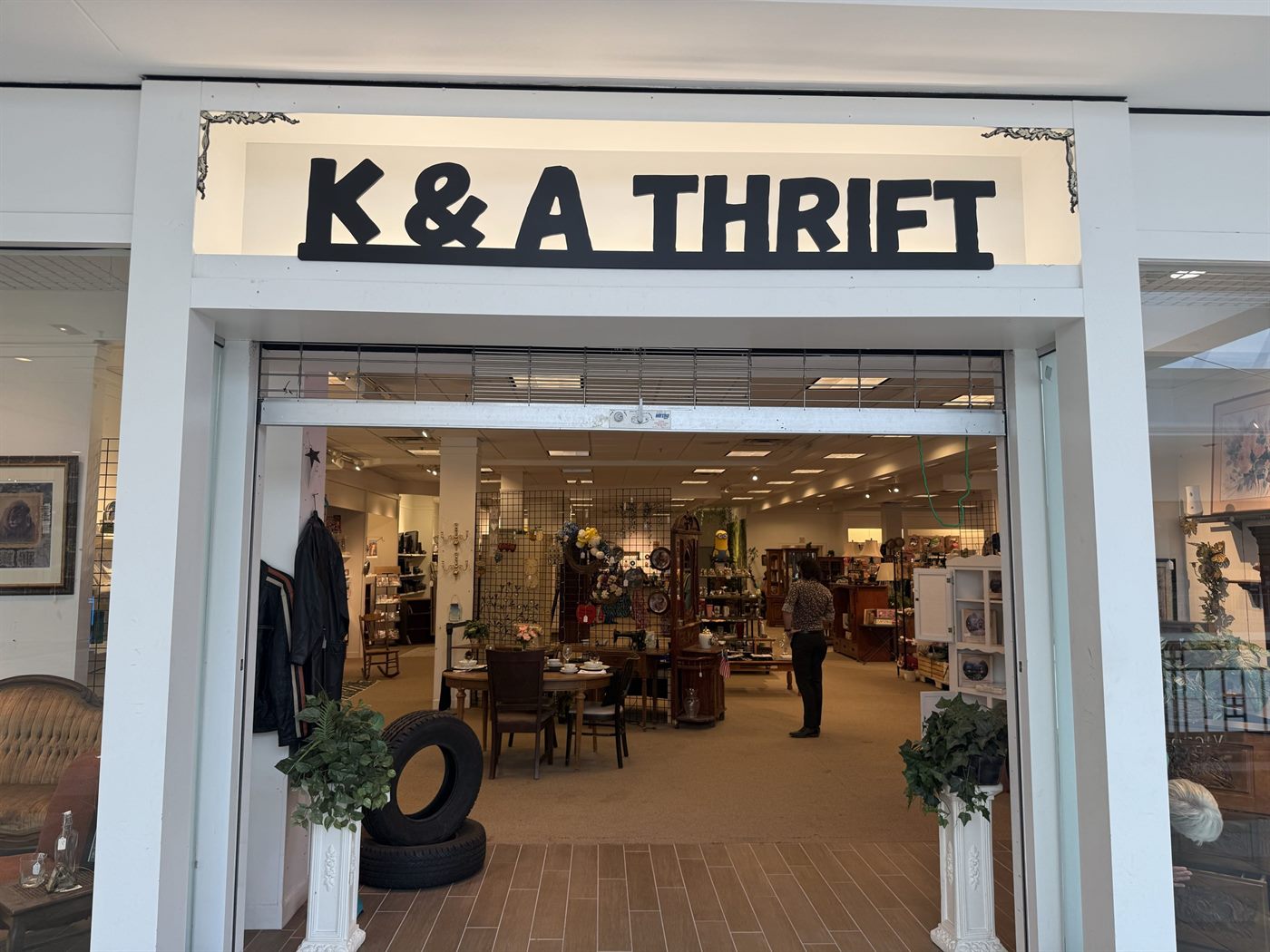 The K&A This & That Thrift entrance seen head-on, with furniture, glassware and a full dining set arranged just inside the doorway